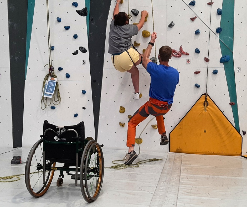 Frau mit körperlicher Behinderung klettert an einer Kletterwand