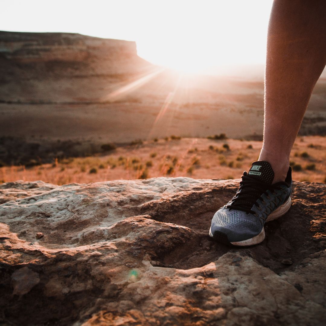 Männliches Bein mit Laufschuh steht auf Berg bei Sonnenuntergang