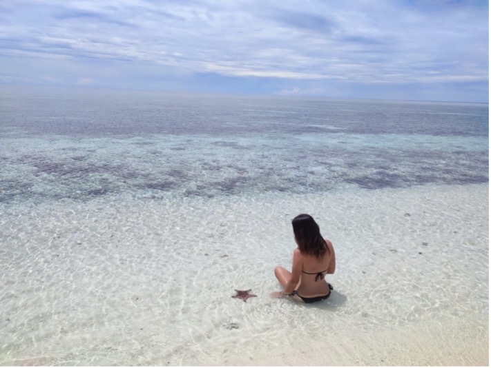 Laura Timm sitzt im Wasser neben einem Seestern auf den Philippinen