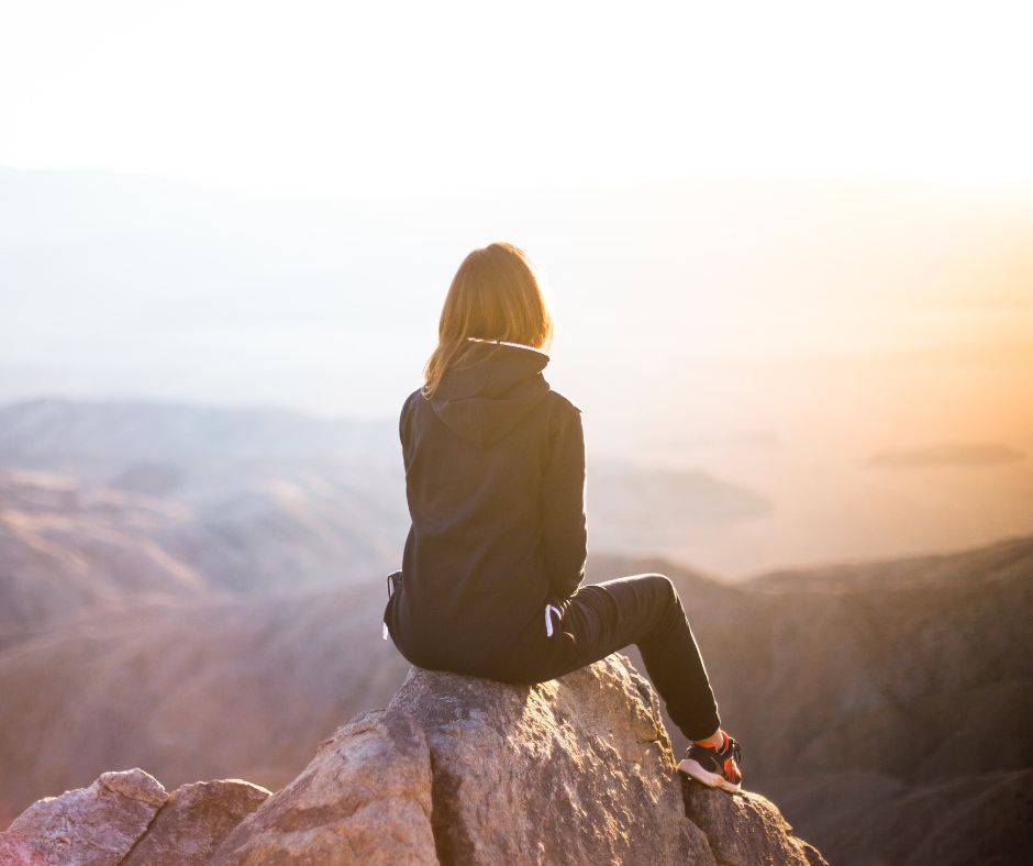 Junge Frau sitzt auf einer Bergspitze und schaut in die Ferne